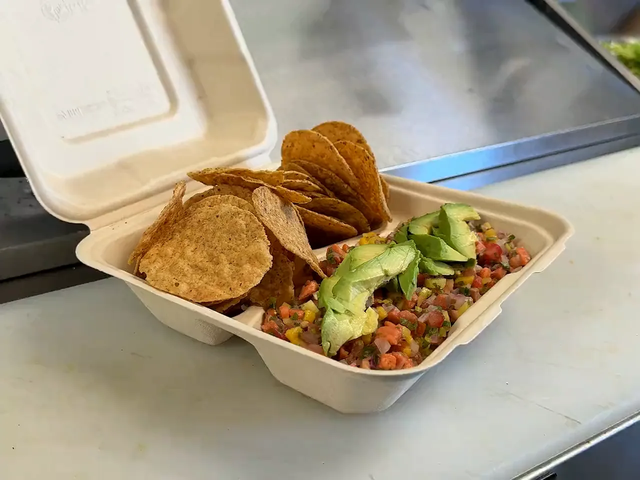 A shrimp ceviche served in a takeout tray with avocado and tostadas
